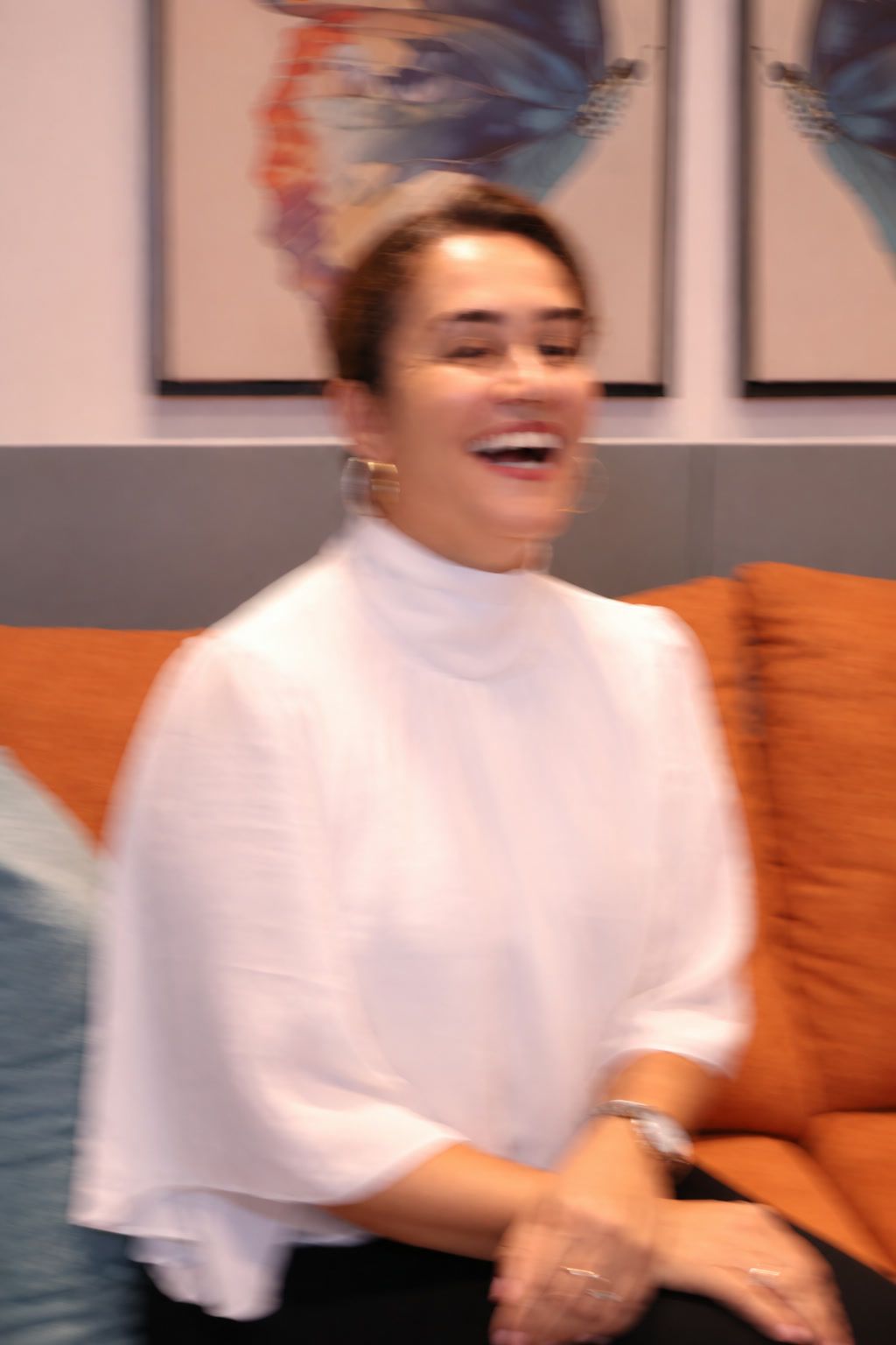 Núbia Paixão rindo, sentada no sofá.